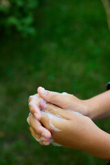 Two hands are rubbing together with soap bubbles while standing outdoors in a green garden. This activity showcases the importance of hygiene and cleanliness.
