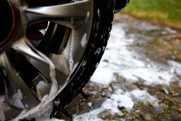 Cleaning car wheel with soap and water in a backyard during a sunny afternoon The suds are visible on the shiny rim.
