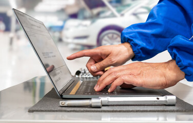 Close-up of hands of manager at the auto repair shop using a laptop in the work place to prepare and tune up a vehicle.