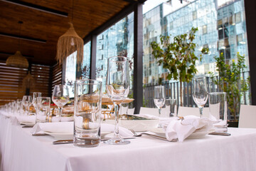 Close-up of table setting: wine glasses, tumblers and white napkins against cityscape backdrop