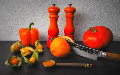 A pumkin, orange pepper belle, physalis fruits on a slate countertop