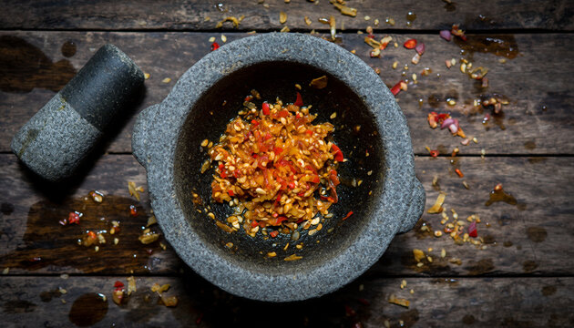 Dark stone mortar filled with crushed red chili peppers and garlic on rustic wood.