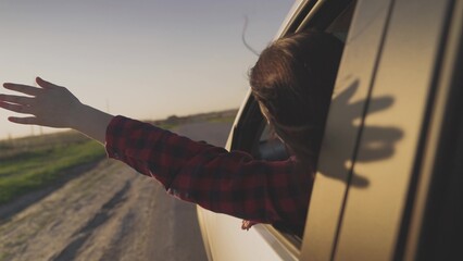 A young girl travels by car on the road, stretch out his hand through the window, catch the wind, enjoying the nature weather, enjoy the freedom of life, travel on a business trip, trip on a voucher.