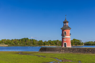 Historical Moritzburg Lighthouse on the shore of the Castle Pond. Red facade and turquoise roof against a blue sky and forest