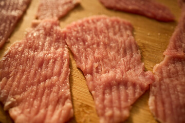 Thin slices of raw meat lay on a wooden cutting board, ready for cooking. The kitchen has warm lighting, creating a cozy atmosphere for meal preparation.