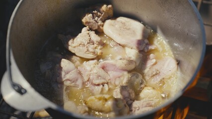 Meat is fried in a pot over an open fire on a camping trip, outdoor recreation with cooking, food on the fire on a day off, a traditional dish with meat, cuisine in extreme conditions.