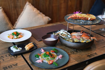Seafood platter with lobster, shrimp, mussels on ice with lemon in restaurant setting. Fresh salad, seafood pasta, creamy sauce on wooden table. Elegant dining experience, gourmet cuisine.
