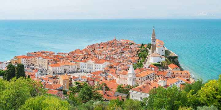 The coastal town of Piran in Slovenia, a picturesque seaside landscape, seen from the Walls of Piran tourist attraction. Colorful buildings surrounded by blue water.