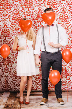 Junge Frau und junger Mann mit roten Herzballons vor roter Tapetenwand
