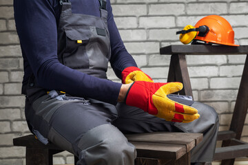 Construction worker putting on protective gloves. Composition with safety equipment.