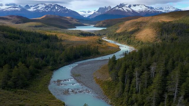 Turquoise river flows through a vibrant green valley in Torres del Paine National Park, Chile, beneath majestic snowy peaks.