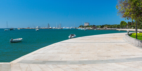 A promenade along a bay with moored boats in the Croatian town of Umag, seen on a sunny summer day.