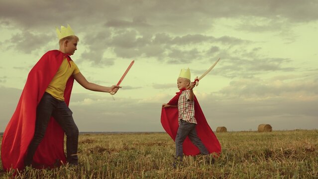 children superheroes play with swords field kings knights. dream childhood. little kid and his brother fearless defenders. teamwork child boys sons. dream adventure red capes at sunset. summer games - Powered by Adobe