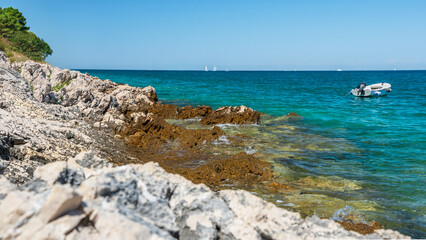 A natural rocky coastline on the shore of the sea with clear blue water. Sharp rocks jut out above...