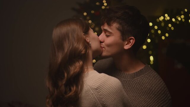A tender holiday moment as a young man gently looks into his partner's eyes before soft Christmas lights, sharing a warm affectionate kiss filled with intimacy and gentle festive emotion.