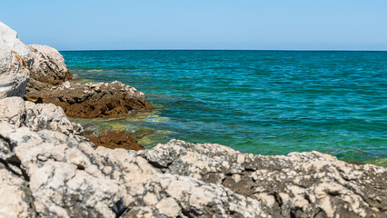 A natural rocky coastline on the shore of the sea with clear blue water. Sharp rocks jut out above...