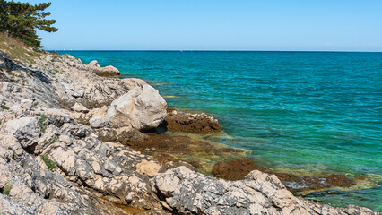 A natural rocky coastline on the shore of the sea with clear blue water. Sharp rocks jut out above...