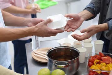 Volunteers giving food to homeless people in shelter, closeup