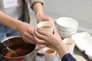 Volunteer giving drink to homeless girl in shelter, closeup