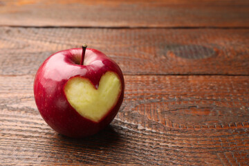 Ripe apple with carved heart on wooden table, closeup. Space for text