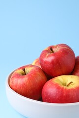 Ripe red apples in bowl on light blue background, closeup. Space for text