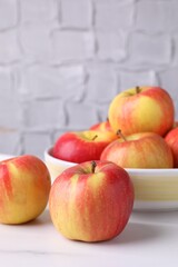 Ripe red apples and bowl on white table near grey textured wall, closeup. Space for text