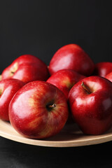 Ripe red apples on wooden table against black background, closeup