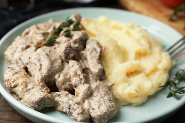Delicious beef stroganoff with mashed potatoes and thyme served on wooden table, closeup