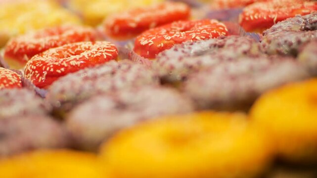 A close-up of delicious donuts with colorful icing. The camera focus slowly pans down the row of sweet pastries. These mouth-watering shots are perfect for food-related projects.