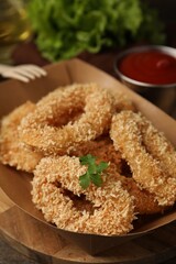 Deep fried squid rings with parsley in takeaway paper box on wooden table, closeup
