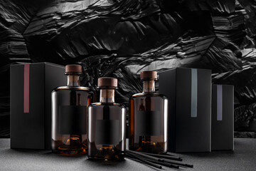 Three glass bottles are placed on a table beside several boxes. Dark sticks are arranged, likely for scent. This arrangement takes place in a space with a dark and textured backdrop.
