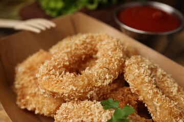 Deep fried squid rings with parsley in takeaway paper box on table, closeup