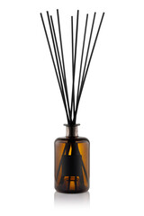 A glass container sits on a table holding several black reeds for scent. The setting is indoors, with a neutral background that highlights the container. This is a common decor item.