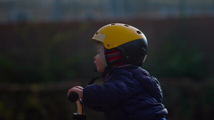 Toddler riding scooter forward in close side view with focused expression and steady motion against soft outdoor background creating gentle moment of early balance practice and smooth movement