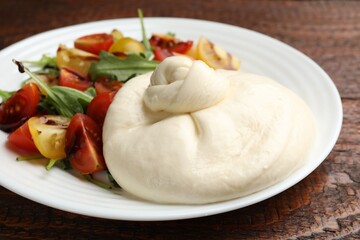 Delicious burrata cheese with tomatoes and arugula on wooden table, closeup