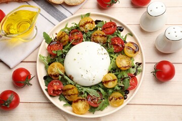 Delicious burrata cheese with arugula, tomatoes and dressing on light wooden table, flat lay