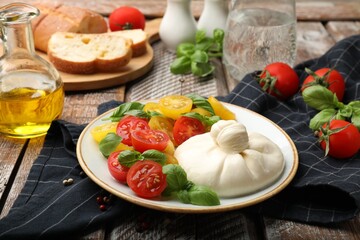 Delicious burrata cheese with basil and tomatoes on wooden table, closeup