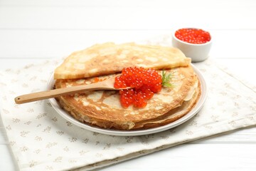 Tasty crepes with red caviar on white wooden table, closeup