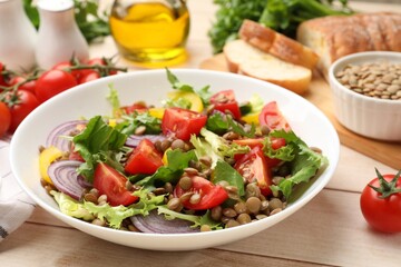 Delicious lentil salad and ingredients on light wooden table, closeup