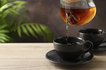 Pouring hot tea into cups from teapot at wooden table, closeup. Space for text