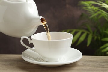 Pouring hot tea into cup from teapot at wooden table, closeup. Space for text
