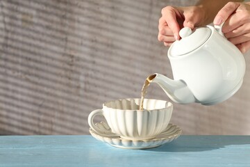 Woman pouring hot tea into cup from teapot at light blue wooden table, closeup. Space for text