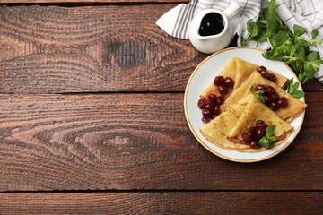 Delicious crepes with cherry jam served on wooden table, flat lay. Space for text