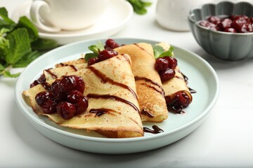 Delicious crepes served with cherry jam and chocolate on white table, closeup