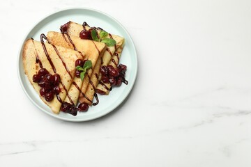 Delicious crepes with cherry jam and chocolate on white marble table, top view. Space for text