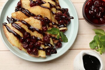 Tasty crepes with cherries, chocolate and mint served on white wooden table, flat lay