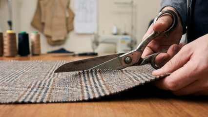 Tailor cutting fabric with a pair of scissors. Craft hobby and sewing workshop. Man creating clothing or repairing textile at a desk.