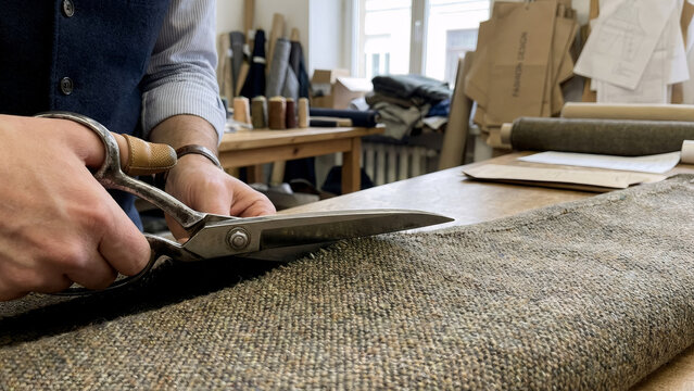 Stock photo close 202511242137 (1) - craftsman cutting tweed fabric. Bespoke tailoring and traditional garment making process. Tailor workshop scene.