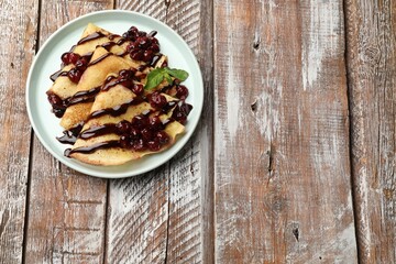 Tasty crepes with cherries, chocolate and mint on wooden table, top view. Space for text