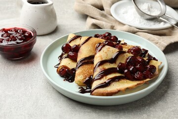 Tasty crepes with cherries and chocolate served on light table, closeup